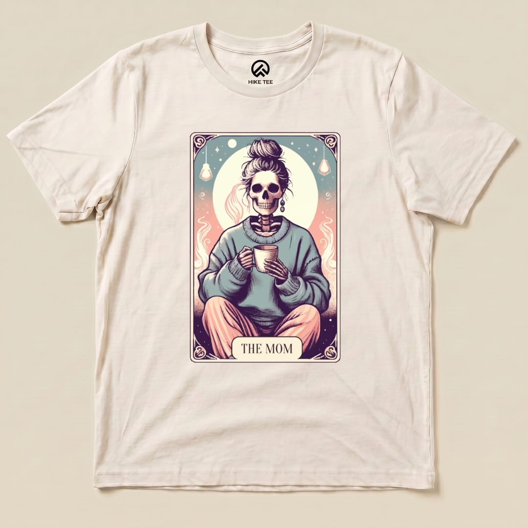 A graphic t-shirt features a whimsical design of a skeleton holding a mug, with the text "THE MOM" below the image.
