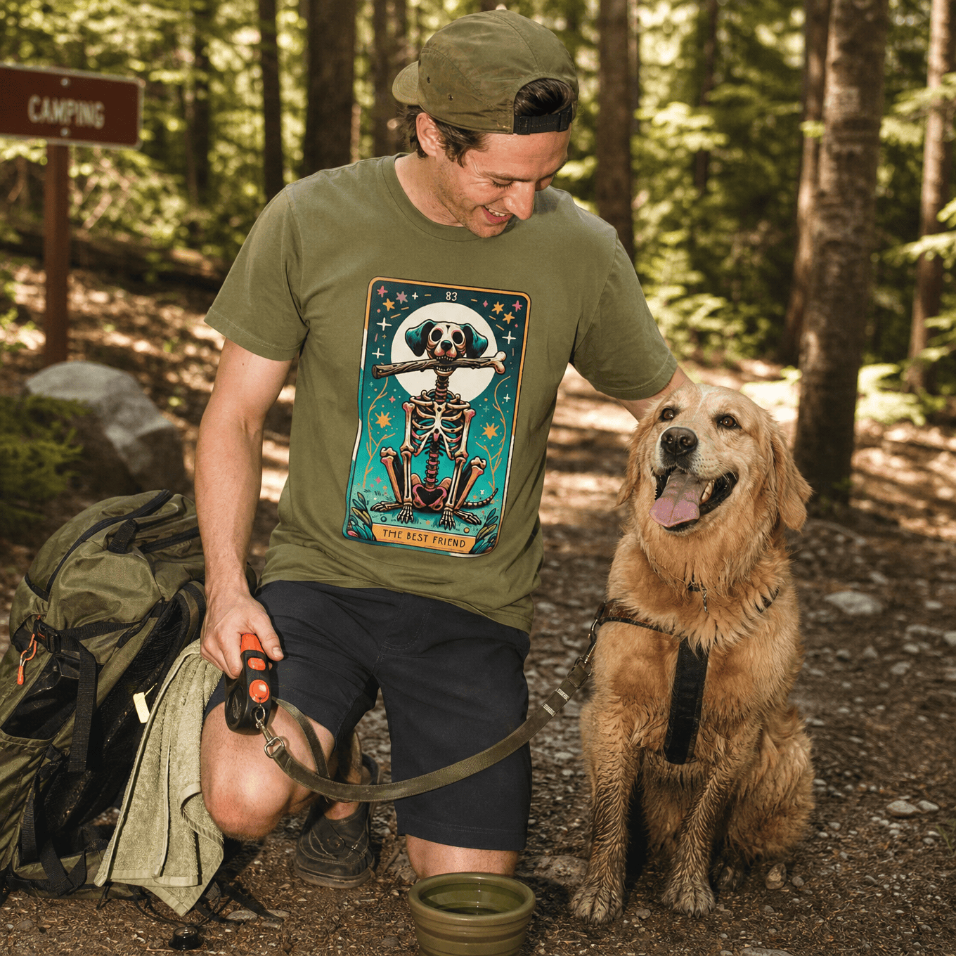 A man kneels in the woods wearing a graphic t-shirt featuring the "Th Best Friend Tarot Card Dog Shirt" design with a playful skeleton.