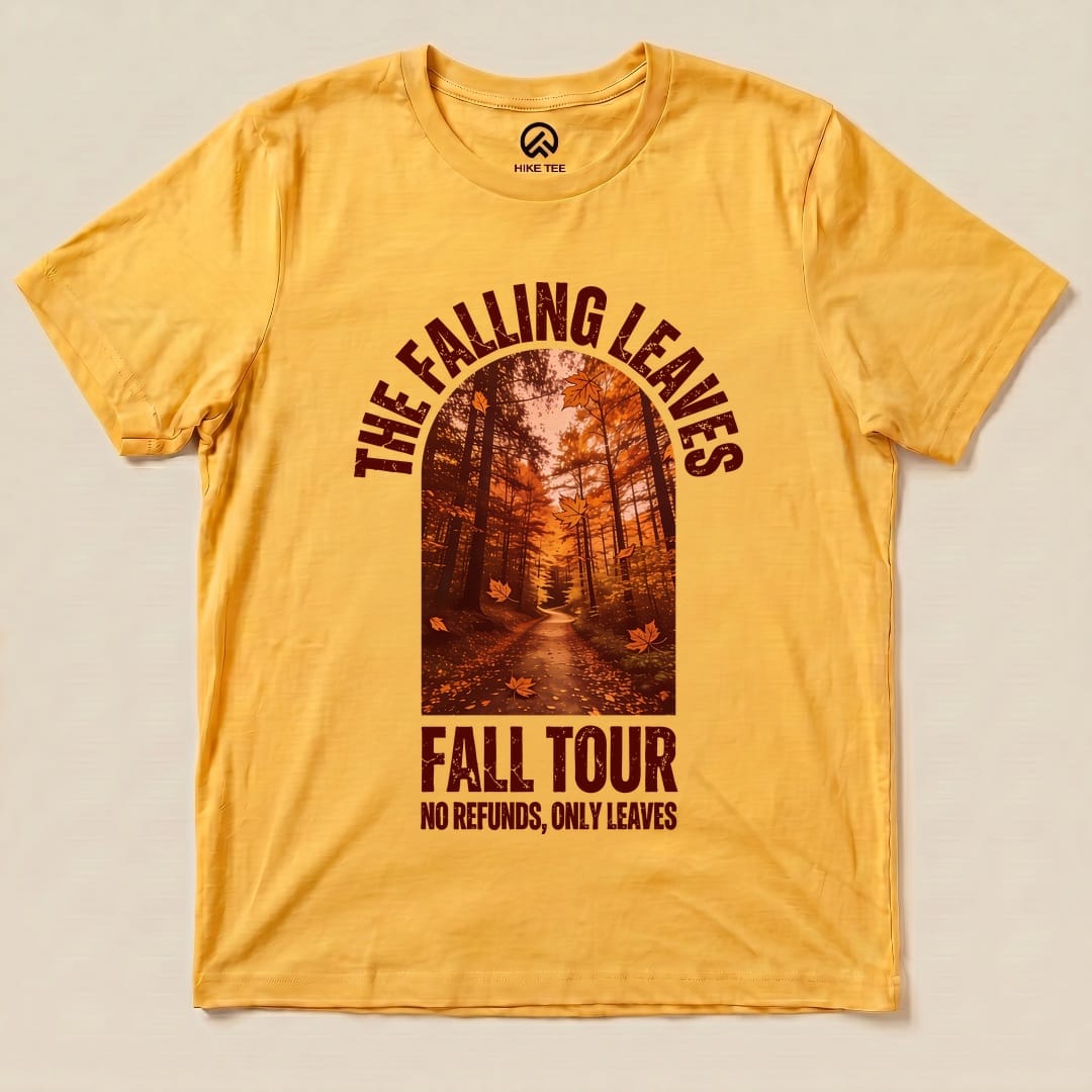 A graphic t-shirt in warm yellow featuring "The Falling Leaves Fall Tour" design with a scenic forest path and autumn leaves.
