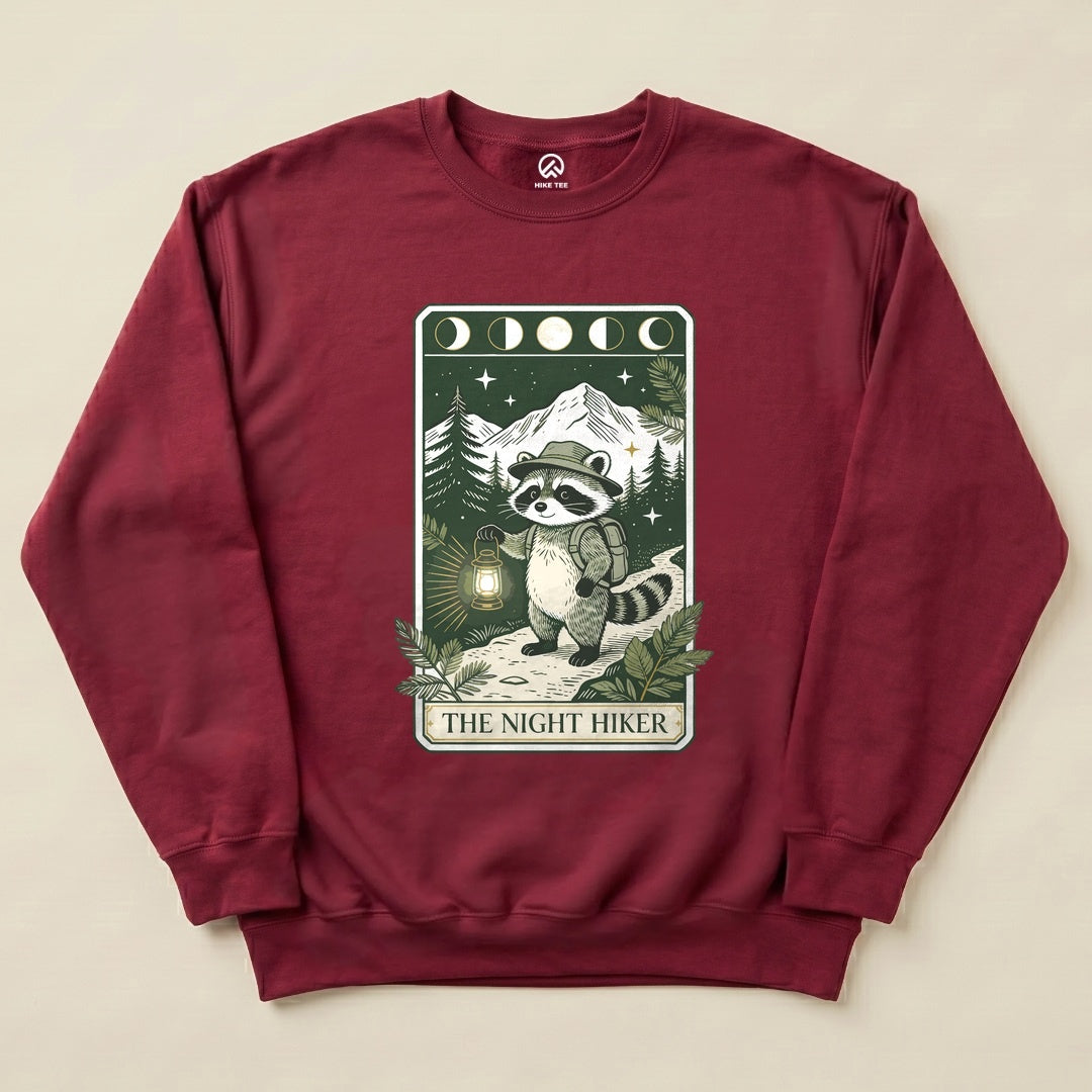 The maroon "The Night Hiker Sweatshirt" features a graphic of a raccoon in a hat with a lantern, set against a mountain backdrop.