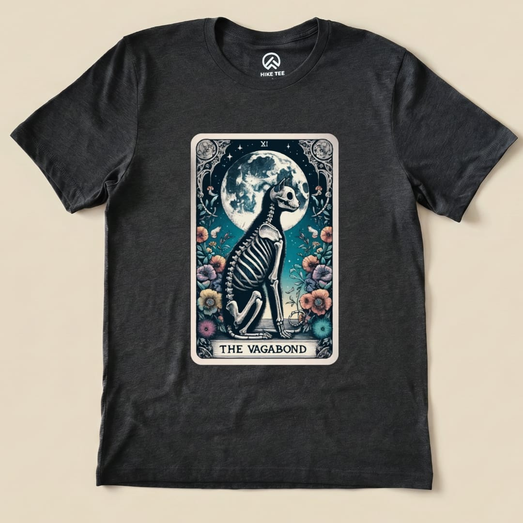 A graphic t-shirt featuring "The Vagabond Tarot Card Cat Shirt" design, showcasing a skeleton cat sitting by a full moon and flowers.