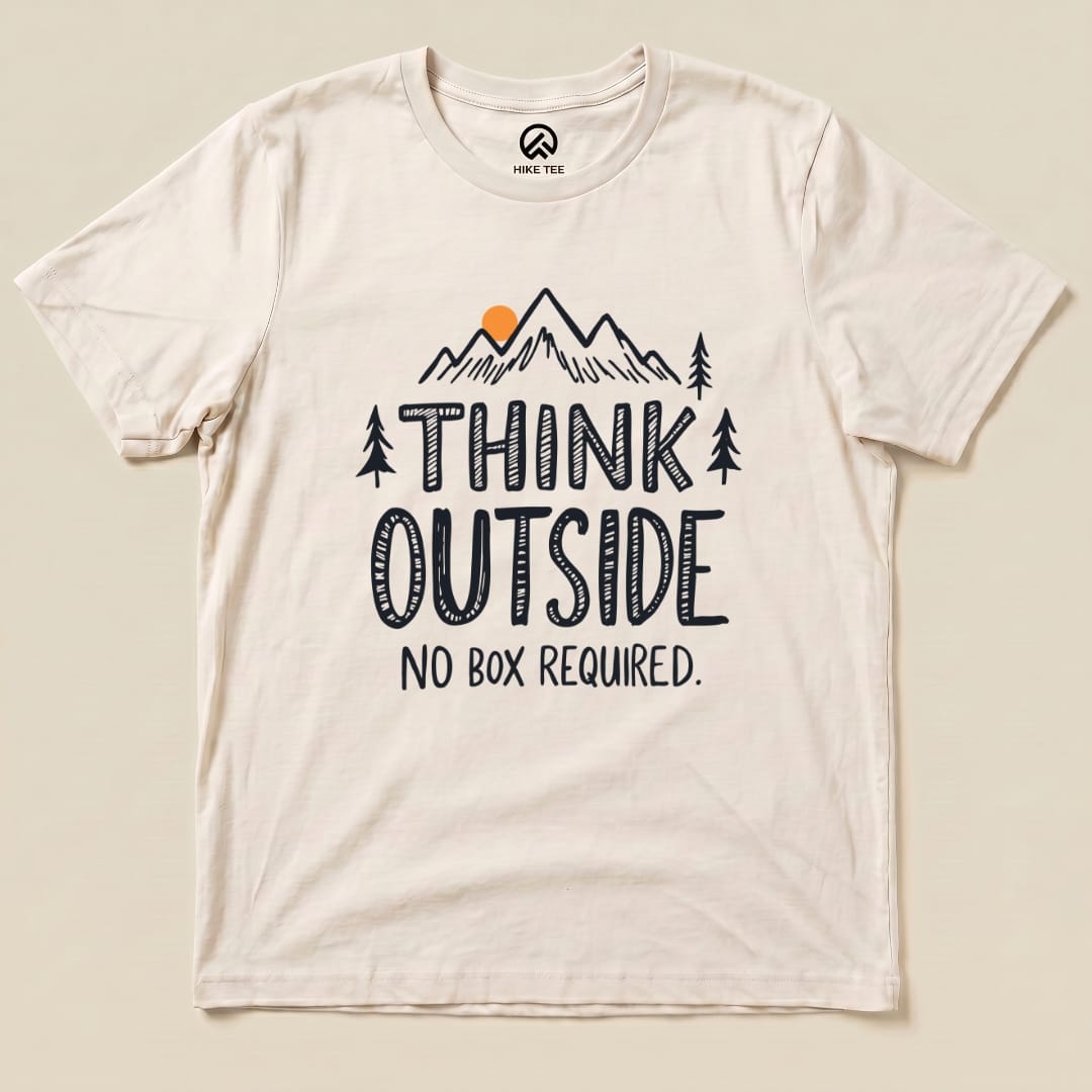A cream graphic t-shirt featuring the slogan "THINK OUTSIDE" above an illustration of mountains and trees, with "NO BOX REQUIRED.