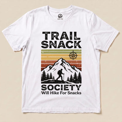 A flat graphic t-shirt features the "Trail Snack Society Shirt" design with a hiker silhouette, mountains, and the phrase "Will Hike For Snacks.