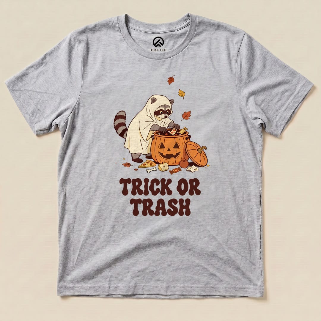 Athletic Heather Trick or Trash Shirt with a raccoon in a ghost costume raiding a pumpkin candy bucket graphic