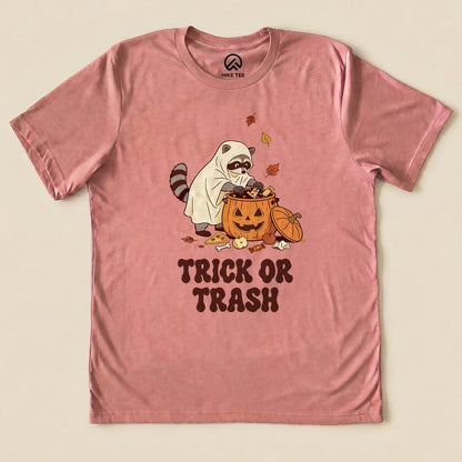Heather Mauve Trick or Trash Shirt with a raccoon in a ghost costume raiding a pumpkin candy bucket graphic