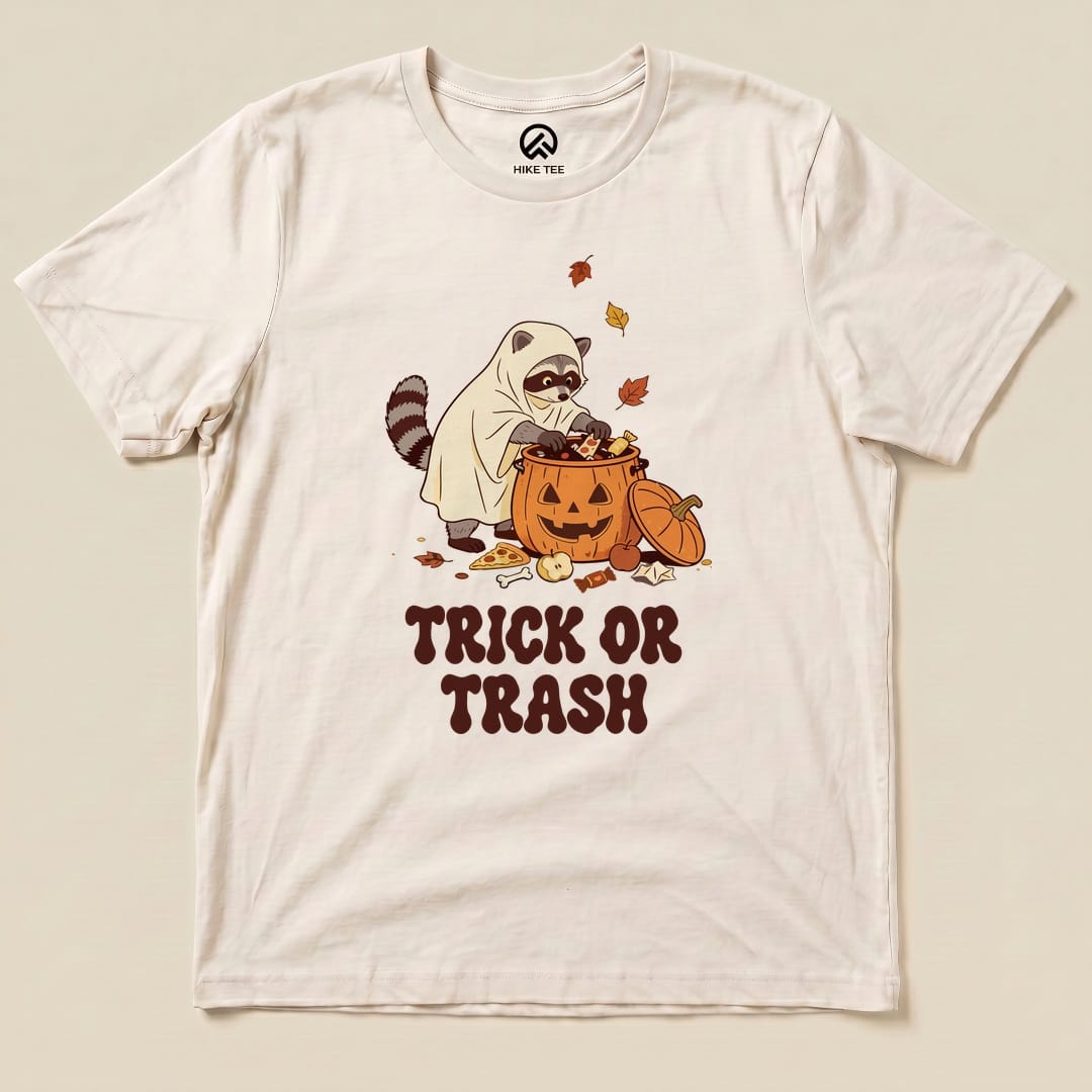 Natural Trick or Trash Shirt with a raccoon in a ghost costume raiding a pumpkin candy bucket graphic