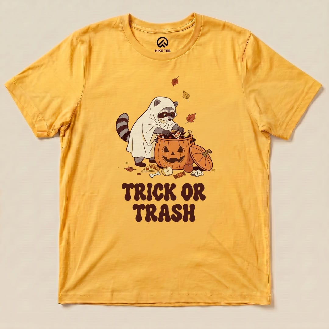 Gold Trick or Trash Shirt with a raccoon in a ghost costume raiding a pumpkin candy bucket graphic