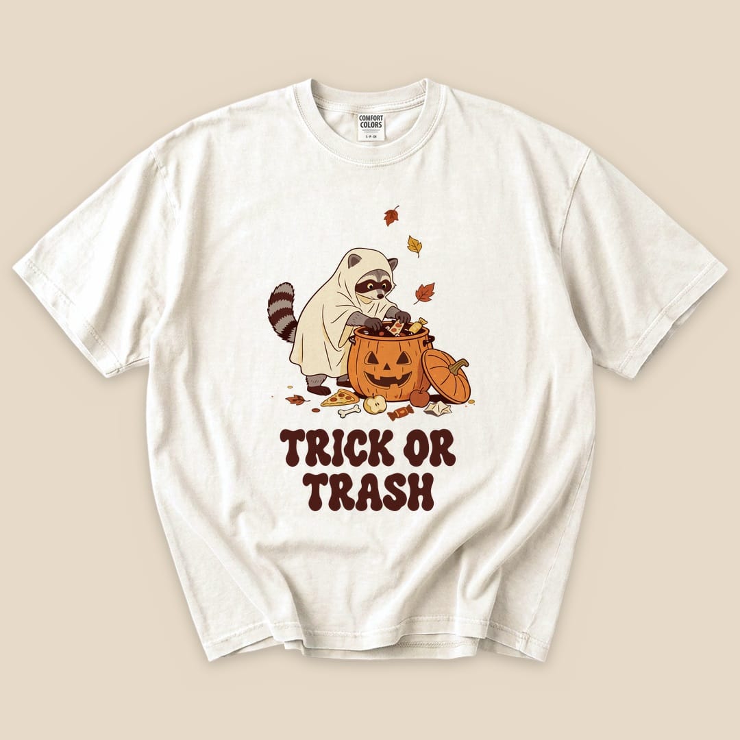 Ivory Trick or Trash T-Shirt with a raccoon in a ghost costume raiding a pumpkin candy bucket graphic