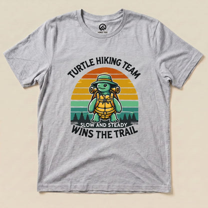 A graphic t-shirt featuring a cheerful turtle in hiking gear, with the phrase "Turtle Wins the Trail" and colorful sunset background.