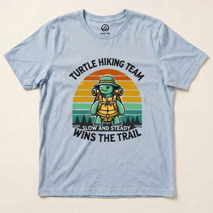 A light blue graphic t-shirt features a turtle wearing a hat and backpack with the slogan "Turtle Wins the Trail.