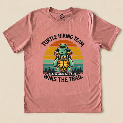 A graphic t-shirt featuring a turtle in hiking gear with the slogan "Turtle Hiking Team Slow and Steady Wins the Trail Shirt.