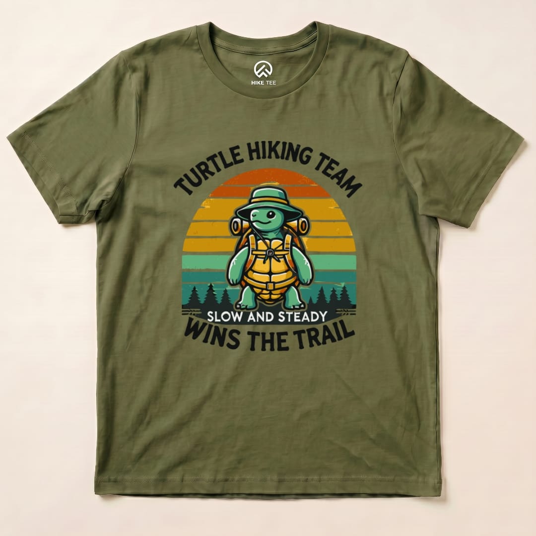 A graphic t-shirt featuring a cartoon turtle with a backpack and the text "Turtle Hiking Team Slow and Steady Wins the Trail.