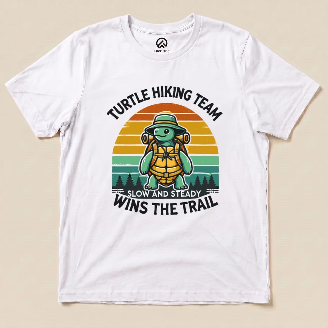 A graphic t-shirt featuring a cartoon turtle in a hiking hat and backpack, with the slogan "Turtle Wins the Trail.