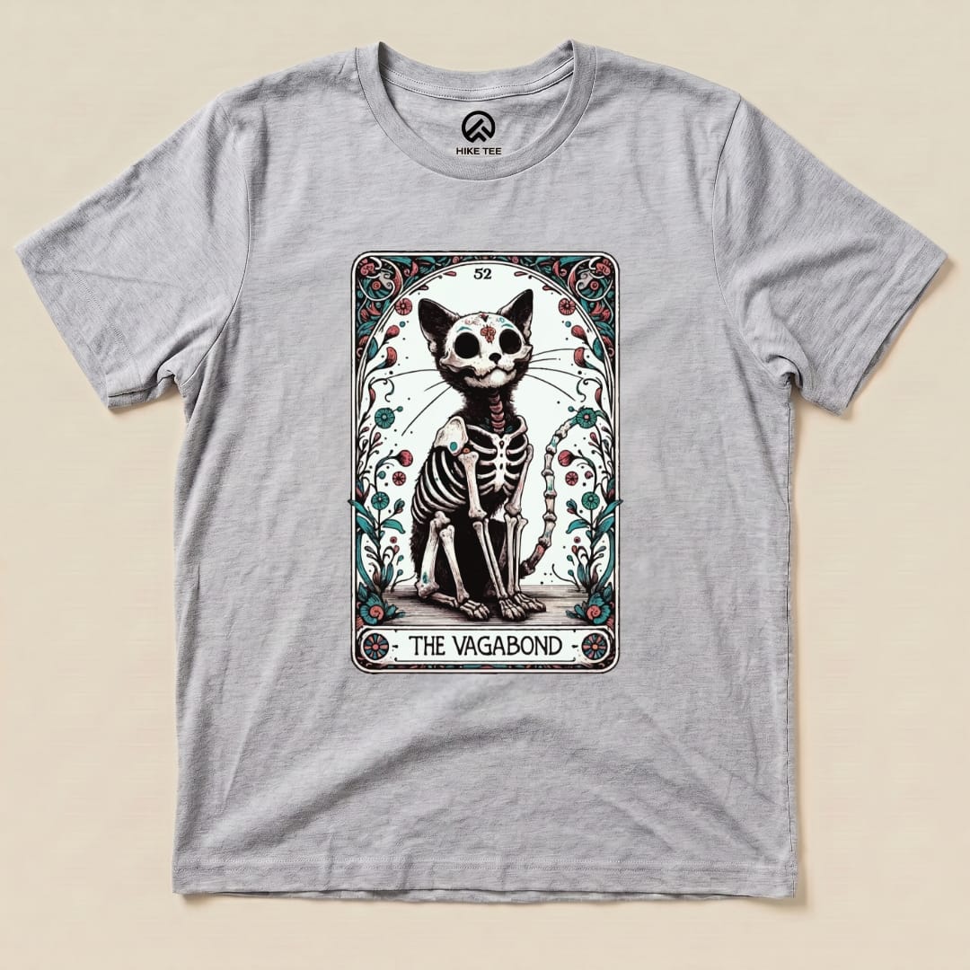 A graphic t-shirt featuring the "Vagabond Tarot Card Cat Shirt," showcasing a skeleton cat design within ornate borders.