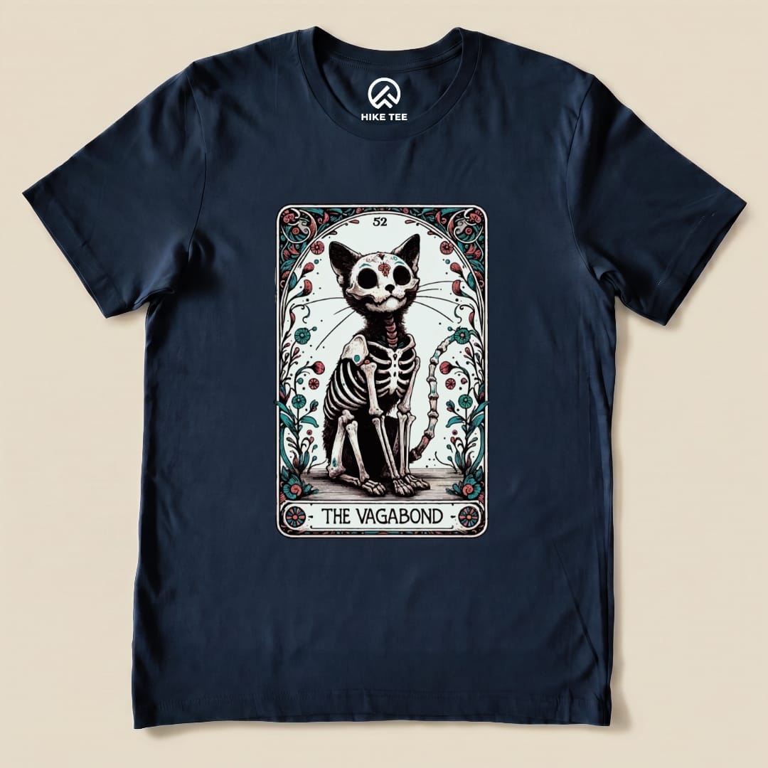 A graphic t-shirt featuring a whimsical skeleton cat illustration framed by floral designs, labeled "THE VAGABOND" beneath it.