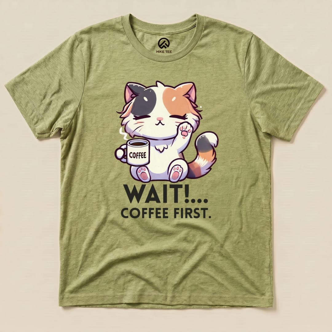 Graphic t-shirt featuring a cute cat holding a coffee cup with the text "WAIT!... COFFEE FIRST." on an olive green background.