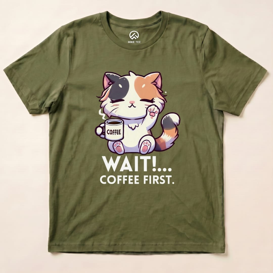 Graphic t-shirt featuring a cute cat holding a coffee cup with the text "WAIT!... COFFEE FIRST" on an olive green background.