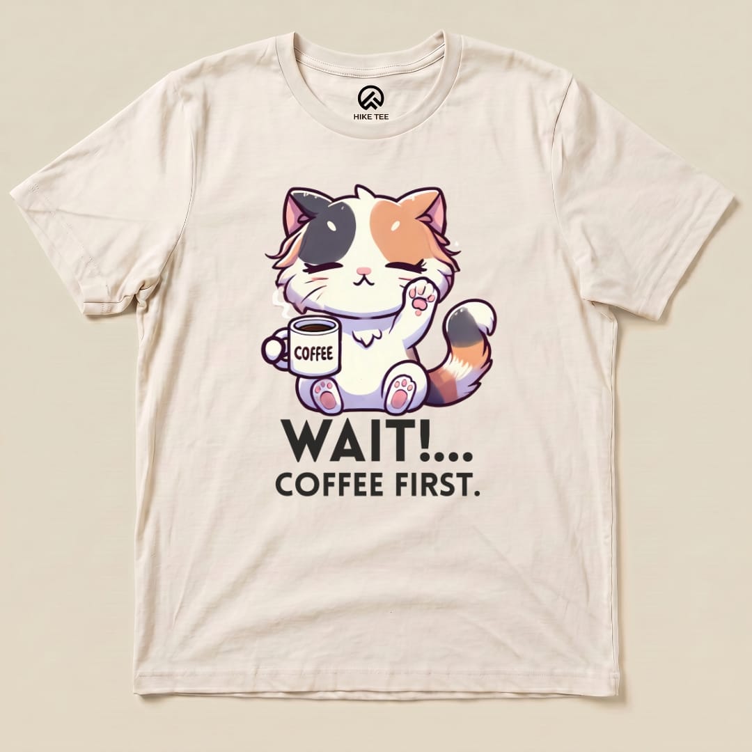 A graphic t-shirt featuring an adorable cat holding a coffee cup and the phrase "WAIT!... COFFEE FIRST.