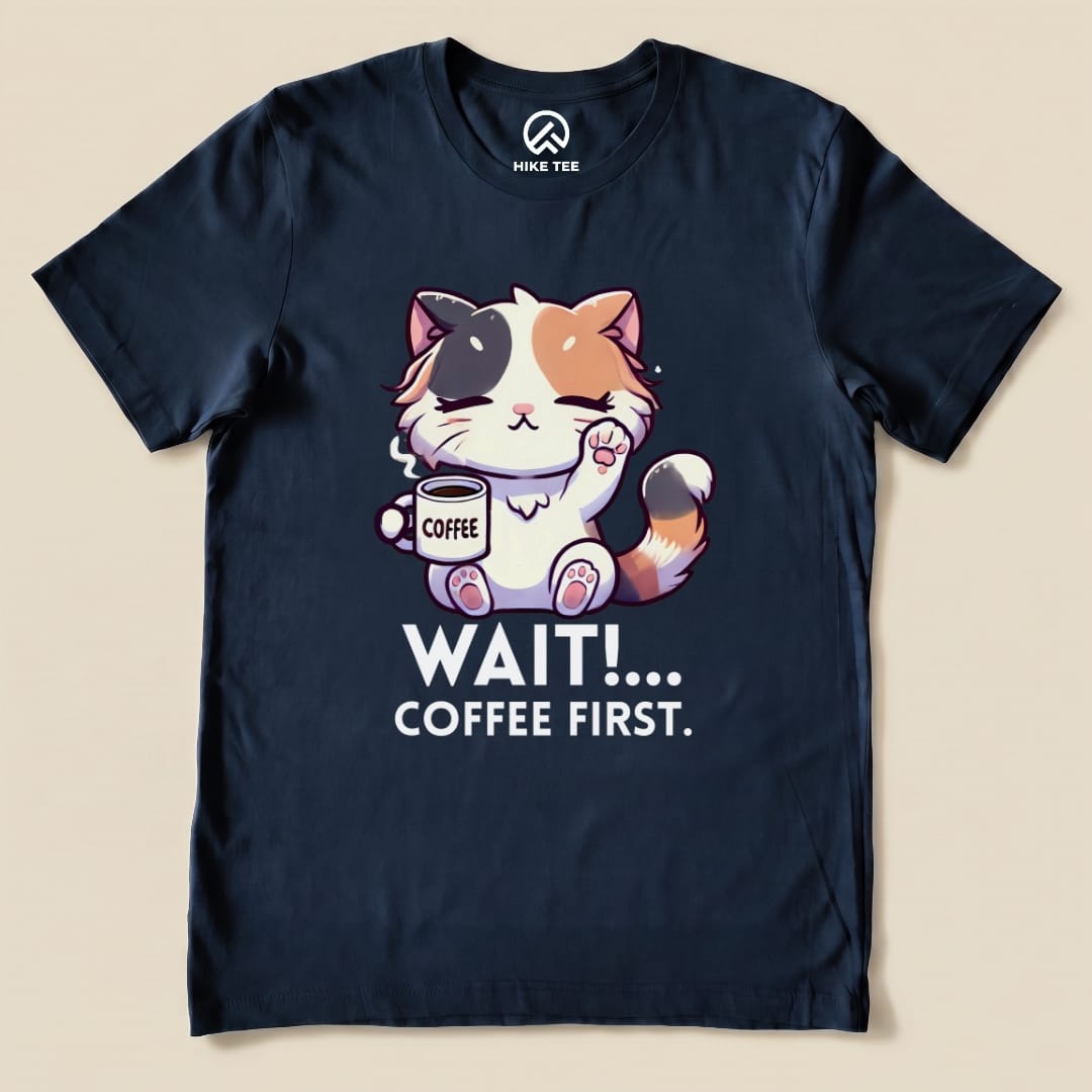 A navy graphic t-shirt featuring a cute cat holding a coffee cup with the text "WAIT!... COFFEE FIRST." printed below.