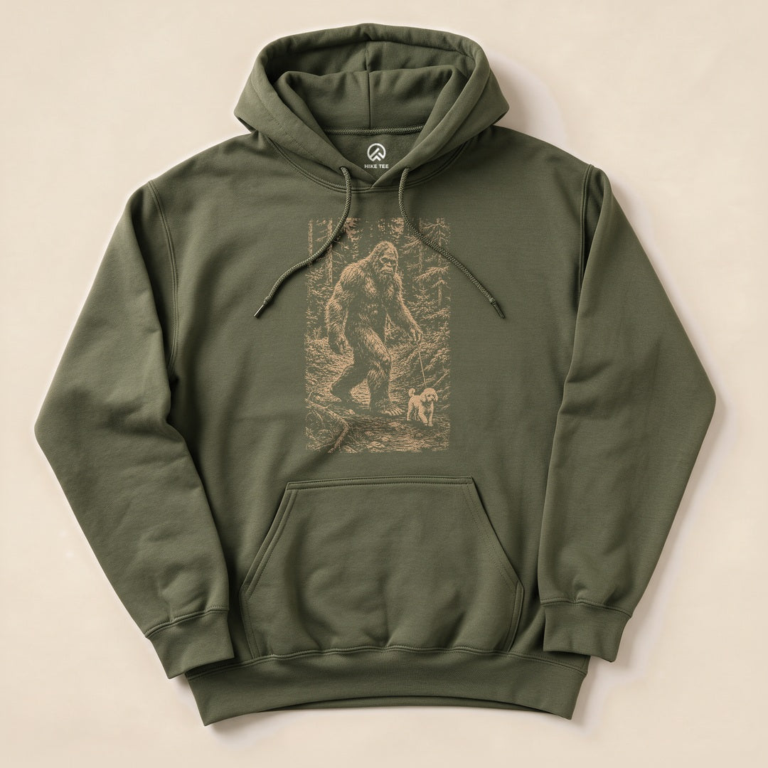 A green "Walking the Dog Hoodie" featuring a graphic of Bigfoot walking a small dog in a forest scene, laid flat on a light background.