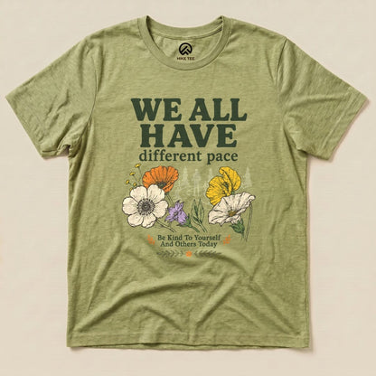 Green graphic t-shirt featuring the slogan "We All Have different pace" with colorful flowers and the phrase "Be Kind To Yourself And Others Today.