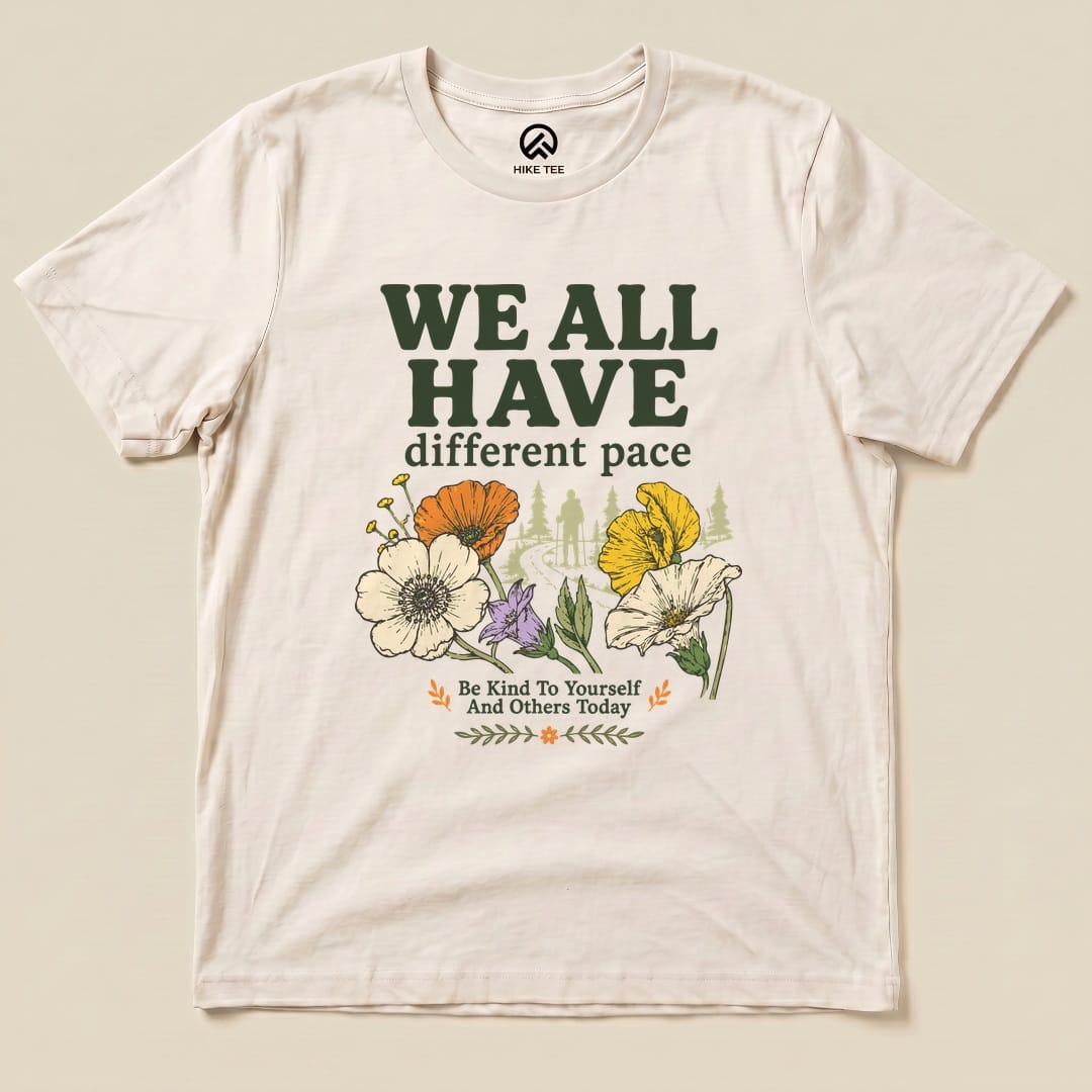 A graphic t-shirt featuring "We All Have Different Pace" in bold text, surrounded by colorful flowers and an outdoor scene.
