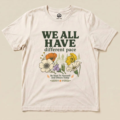 A graphic t-shirt featuring "We All Have Different Pace" in bold text, surrounded by colorful flowers and an outdoor scene.