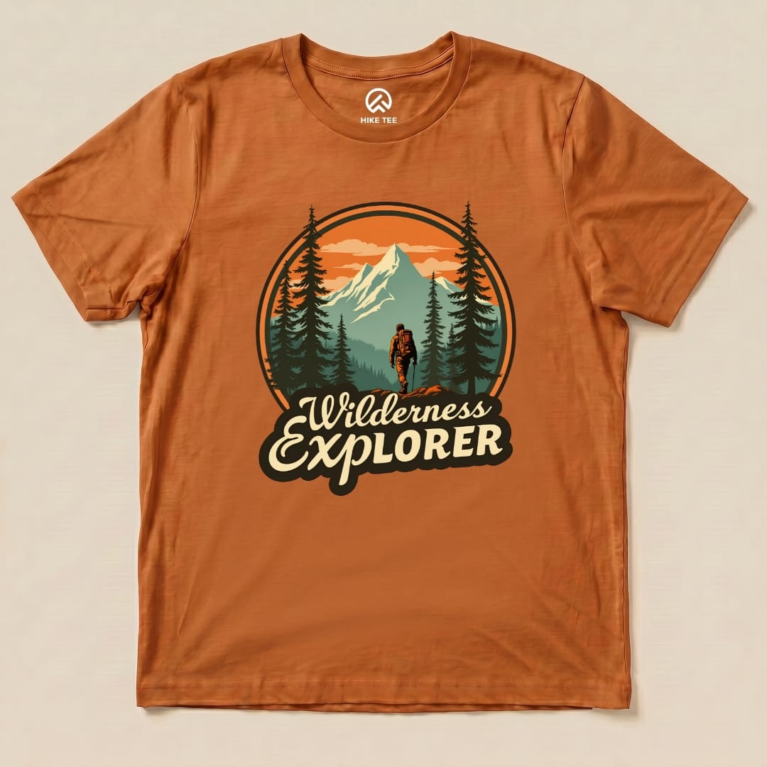 A graphic t-shirt in earthy tones featuring a hiker surrounded by trees and mountains, labeled "Wilderness Explorer Shirt.