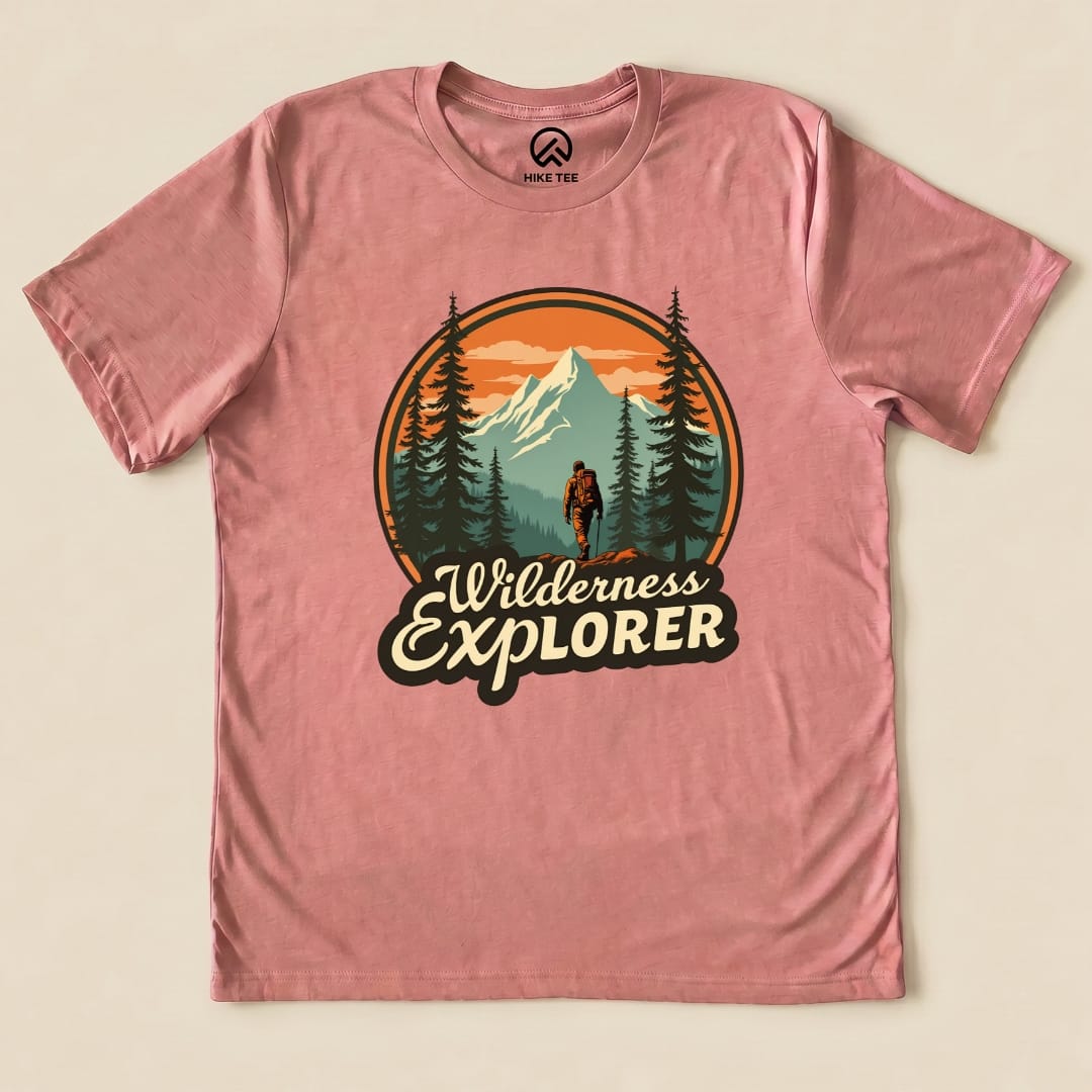 A graphic t-shirt in pink featuring a hiker amidst mountains and trees, with the words "Wilderness Explorer" prominently displayed.