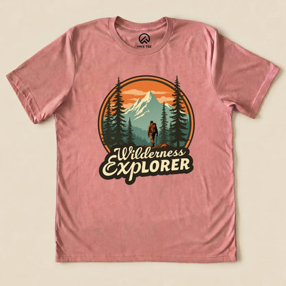 A graphic t-shirt in pink featuring a hiker amidst mountains and trees, with the words "Wilderness Explorer" prominently displayed.