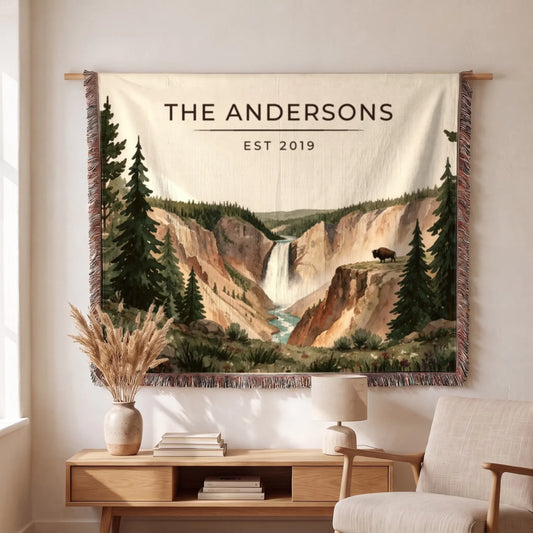 A beautifully woven Yellowstone Falls Bison Woven Blanket displays a tranquil waterfall scene with a bison and lush greenery.