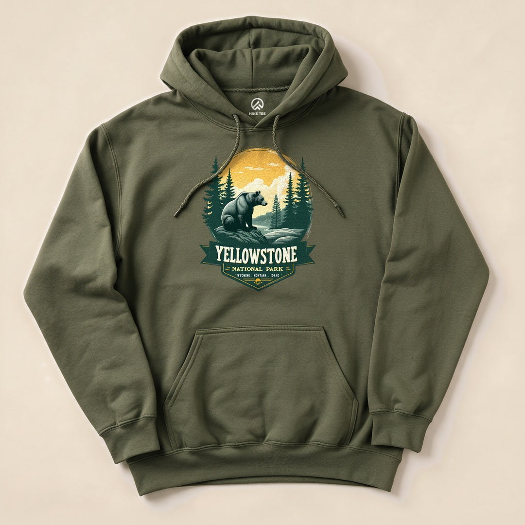 A graphic hoodie featuring a Yellowstone Grizzly Bear design with a bear, forest, and sun against an olive background.