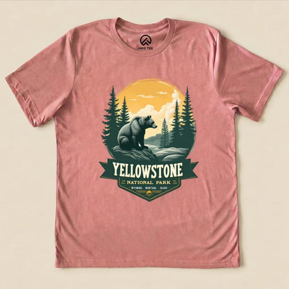 A pink graphic t-shirt features a Yellowstone Grizzly Bear Shirt design with a bear, forest, and sunset in a national park theme.