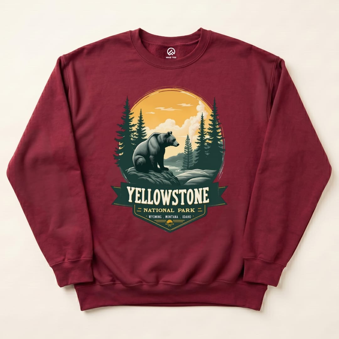 A maroon Yellowstone Grizzly Bear Sweatshirt features a graphic of a bear in a forest setting under a sunset with "Yellowstone National Park" text.