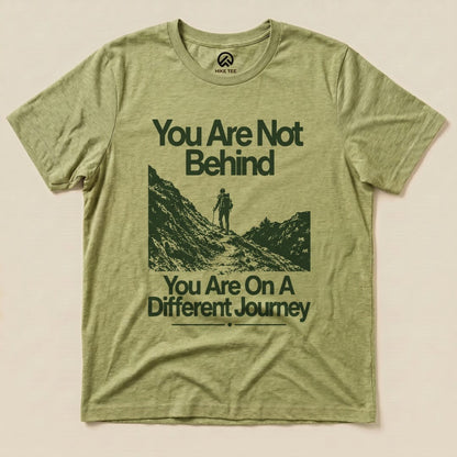 Graphic t-shirt featuring the slogan "You Are Not Behind, You Are On A Different Journey" with a hiker silhouette against a mountain backdrop.