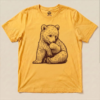 A yellow graphic t-shirt displays an illustration of a cute bear sitting and holding its foot, labeled as a Youth Bear Shirt.