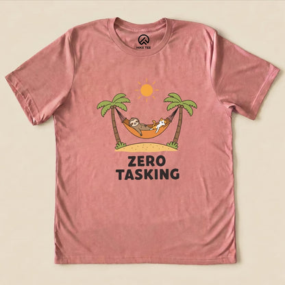 A pink graphic t-shirt featuring a sloth and a cat lounging in a hammock under palm trees, with the phrase "ZERO TASKING.