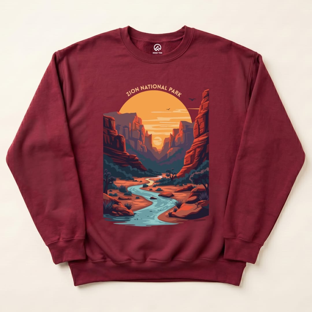 A maroon Zion National Park sweatshirt features a scenic graphic of a river flowing through canyon walls at sunset.